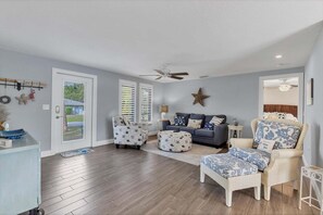 Ein Wohnzimmer mit einer Couch, Hocker und Sessel, einem Deckenventilator und einer Sternen-Dekoration an der Wand.