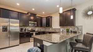 A modern kitchen with dark cabinets, stainless steel appliances, a granite countertop, and a bar area with leather chairs. - Mvp9018sdcg (Davenport)