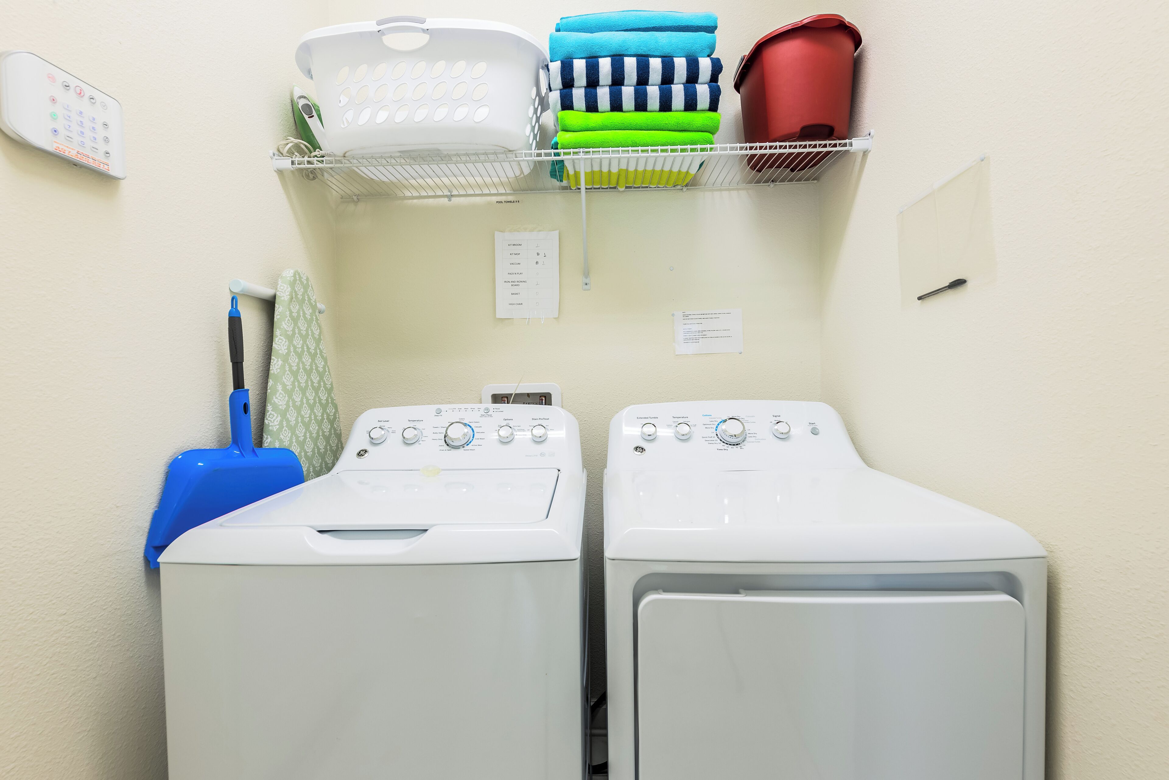 A laundry area with two front-loading washing machines, a drying rack, and a wall-mounted control panel.