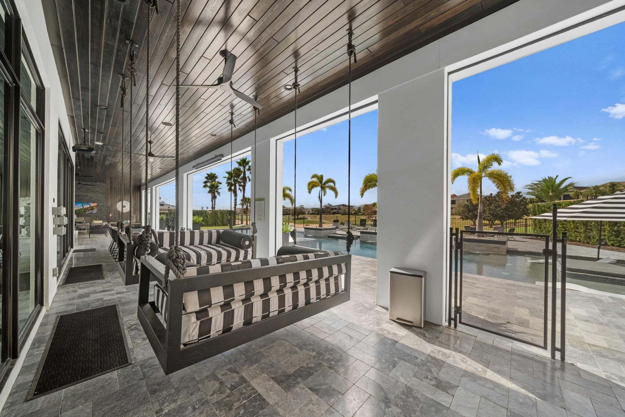 A modern outdoor lounge area with a pool, large windows, and a view of palm trees.
