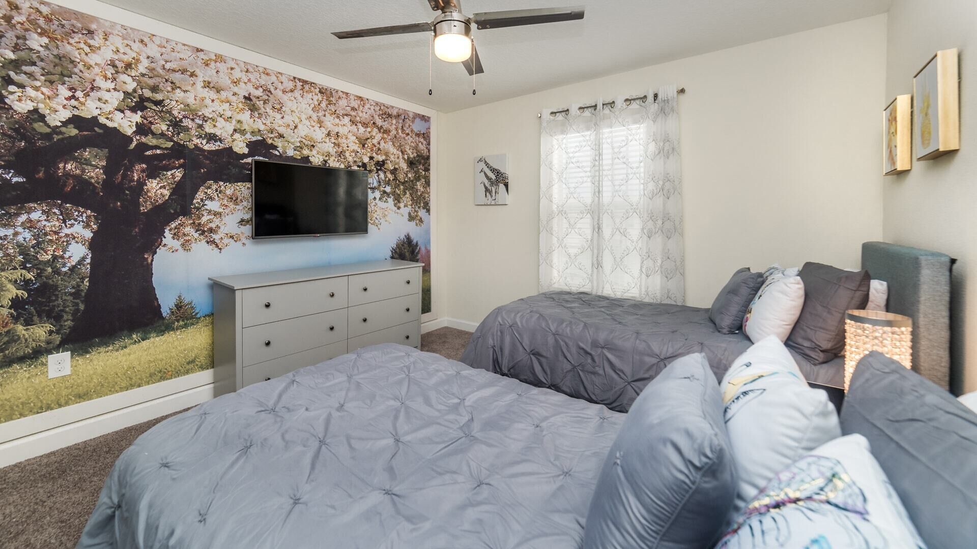 A bedroom with two beds, a TV, a ceiling fan, and a mural on the wall.