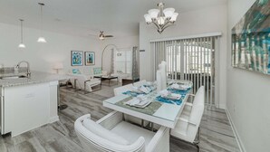 A modern kitchen with a granite countertop, white cabinetry, and a dining area with a glass table set for four. - Mvd1595 (Davenport)