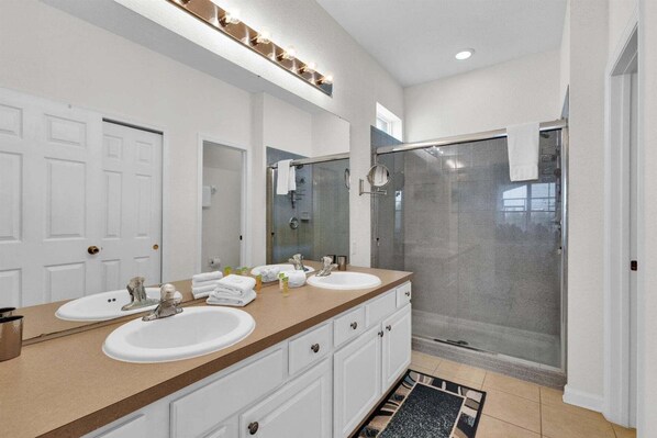 A bathroom with two sinks, a shower, and a mirror with lights. - Windsor Hills Resort 5 Bedroom Updated Pool Home 0853 (Kissimmee)