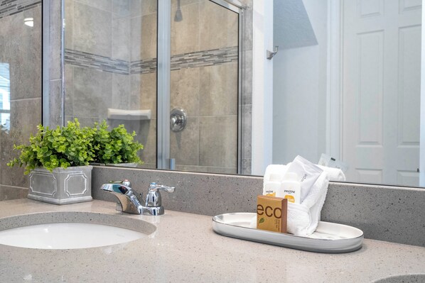 A bathroom with a sink, mirror, and shower area. - Tvpm-2174cb (Kissimmee)