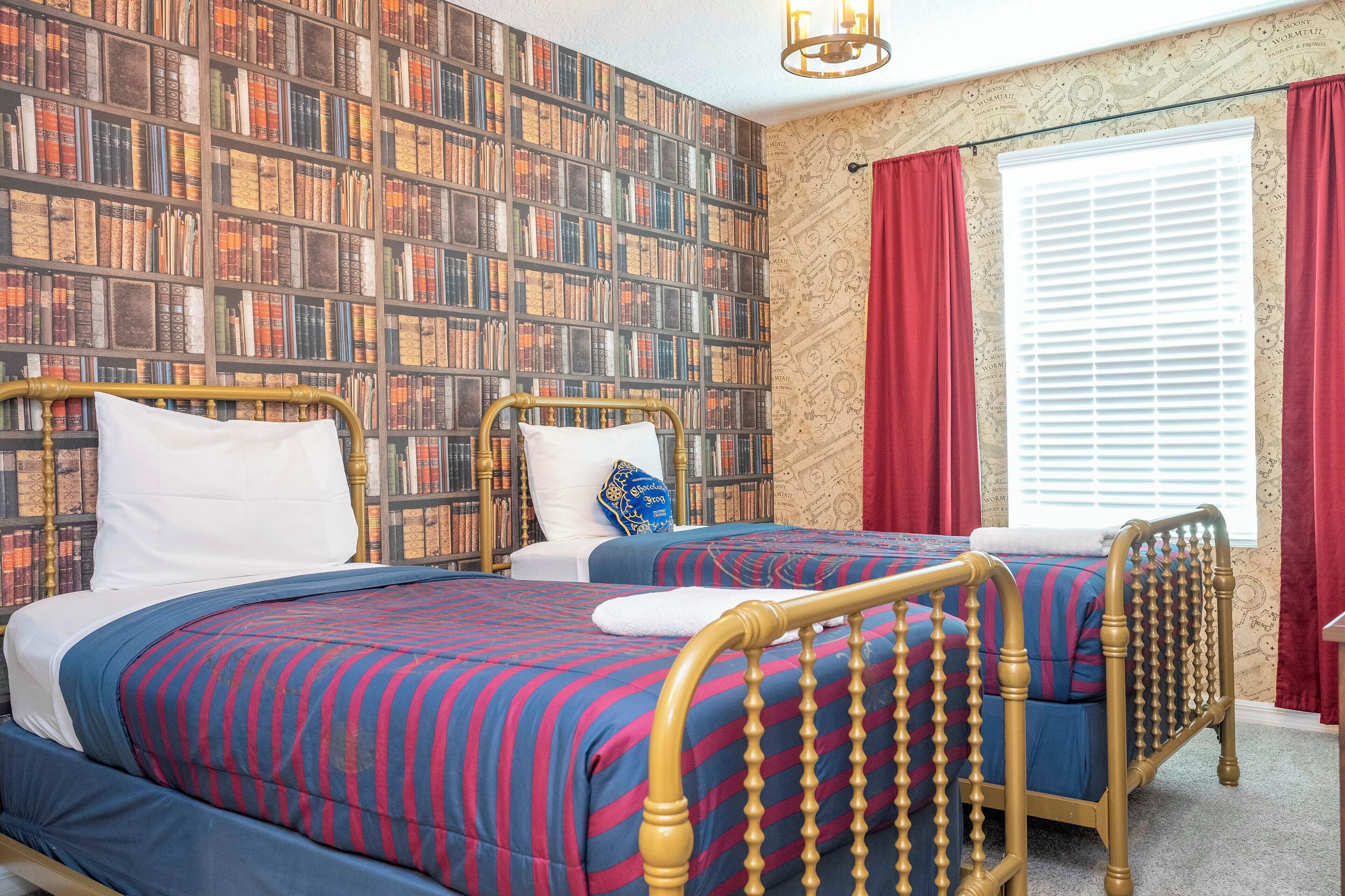 Una habitación con dos camas, una estantería y un ventanal con cortinas.