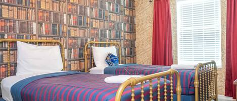 Una habitación con dos camas, una estantería y un ventanal con cortinas.
