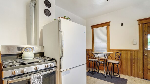 A kitchen with a stove, oven, refrigerator, and a small dining area with chairs and a table. - Historic Downtown Meets Modern Comfort (Colorado Springs)