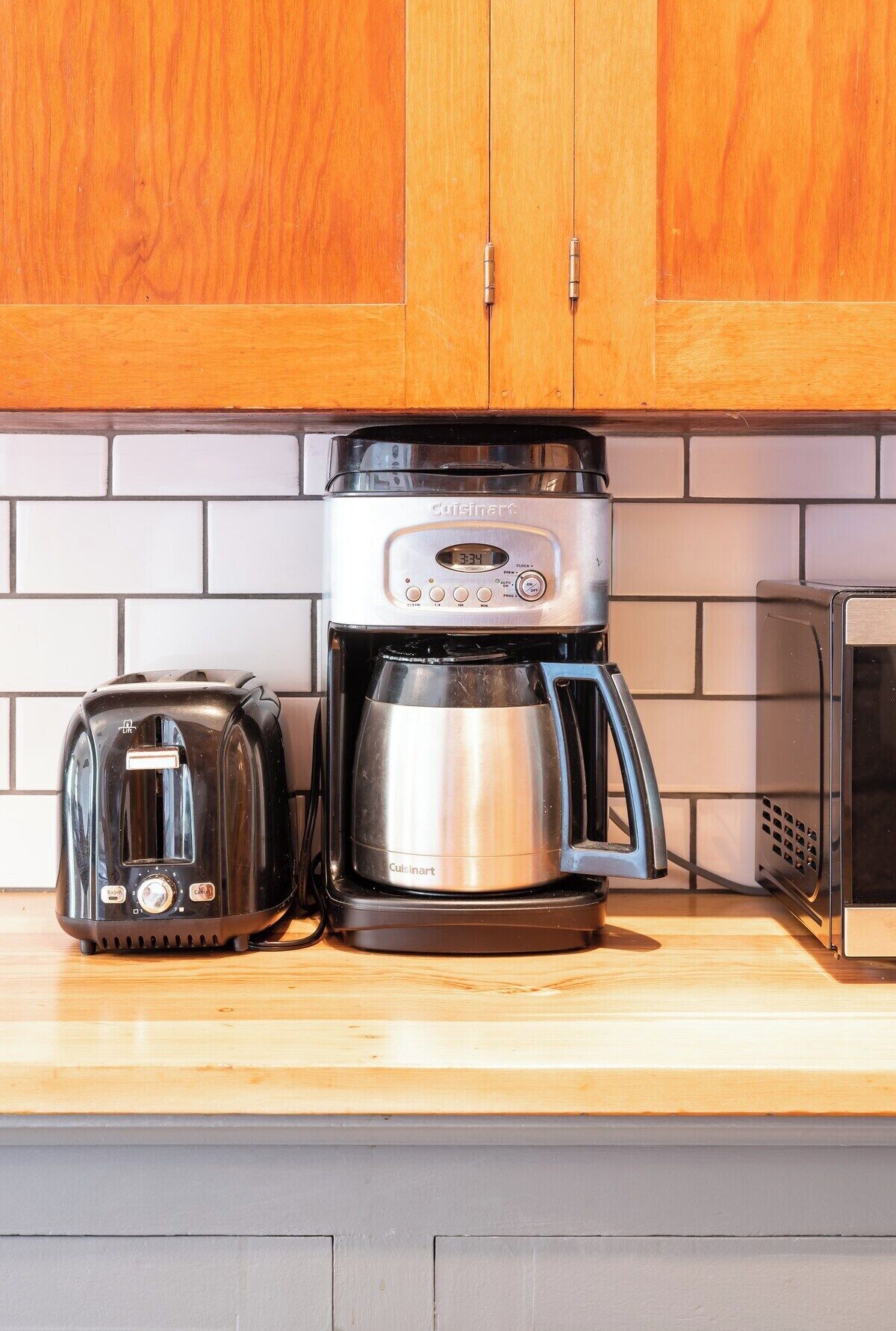 A kitchen with a Cuisinart coffee maker, a toaster, and a microwave on a wooden countertop.