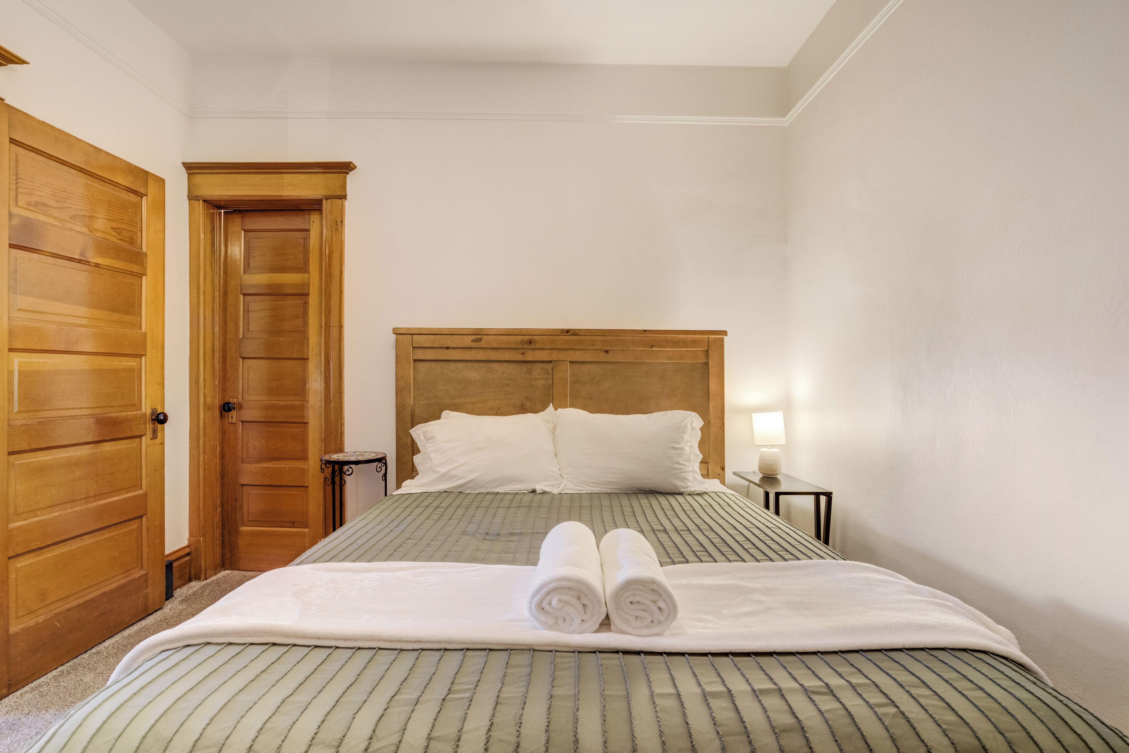 Un lit bien fait, recouvert d’une couvre-lit à rayures, avec une tête de lit en bois et deux serviettes enroulées posées sur le lit.