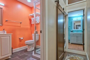 A bathroom with an orange wall, a glass shower enclosure, a white toilet, and a sink with a mirror. - Bright Modern Loft for Adventurers (Roanoke)