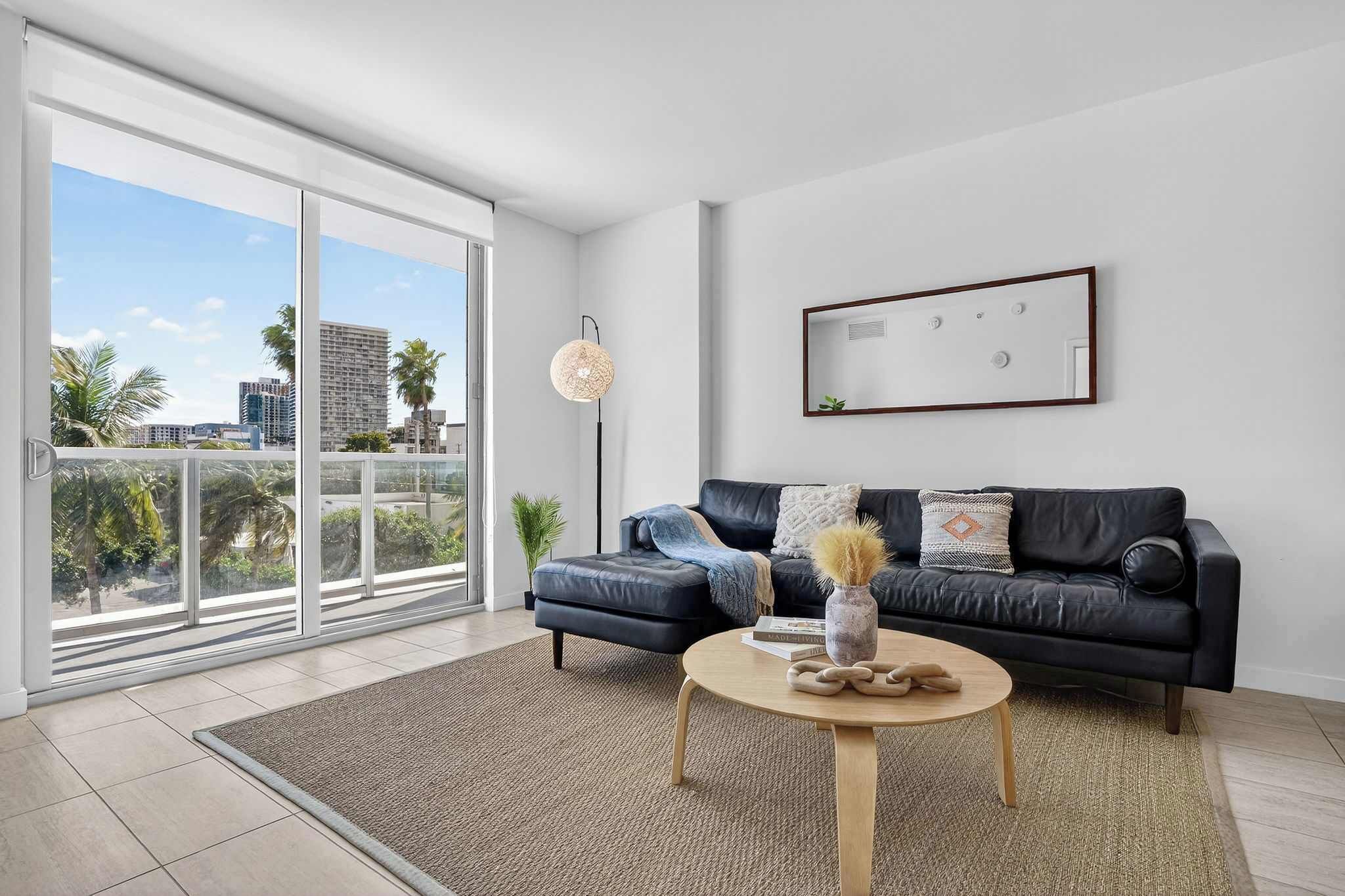 Ein modernes Wohnzimmer mit einem schwarzen Ledersofa, einem runden Couchtisch und einem großen Fenster mit Blick auf die Stadt.