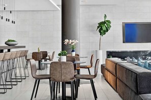 Un espace repas moderne avec une table ronde, des chaises rembourrées, une grande plante et un téléviseur fixé au mur.