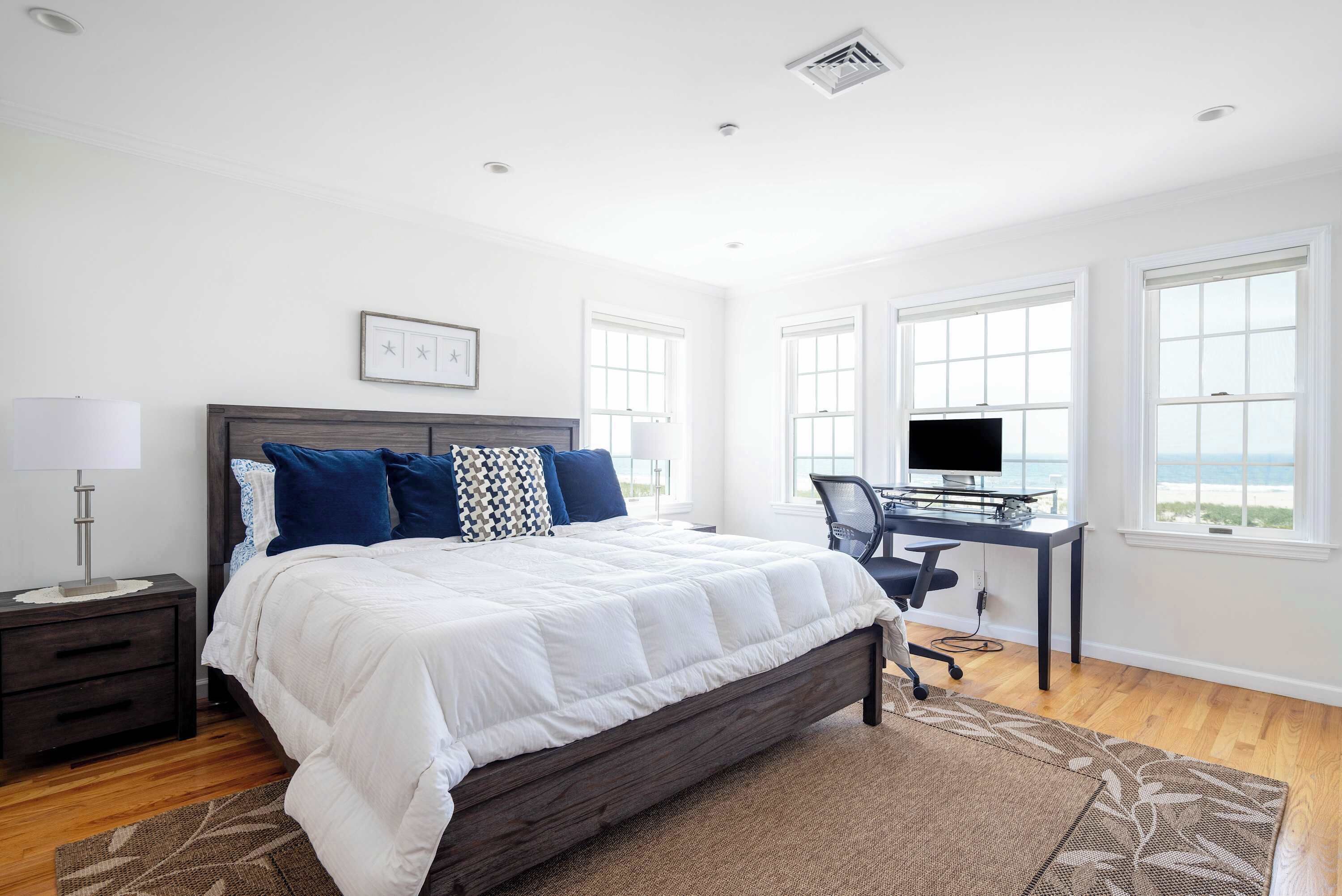 A bedroom with a bed, a desk, and a view of the ocean.