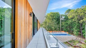 Un edificio moderno con fachada de vidrio, piscina y terraza de madera con vistas a un bosque.