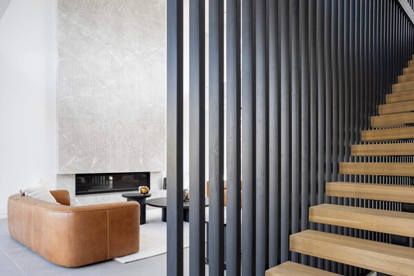 Un intérieur moderne avec un canapé en cuir aux lignes courbes, une cheminée et un escalier avec des marches en bois.