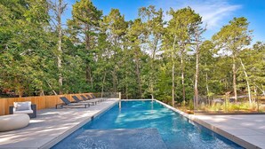 Una piscina rectangular de aguas cristalinas y color azul, rodeada por una terraza de madera y sillones de descanso.