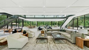 A spacious living area with a large sectional sofa, a coffee table, and a piano. - Glass House by Rove Travel Heated Pool & Hot Tub (East Hampton)