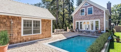 Una casa de dos pisos con piscina, revestimiento de madera y un porche cubierto.