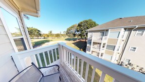 Un balcon donnant sur un terrain de golf, un immeuble doté de nombreux balcons et un ciel d’un bleu limpide.