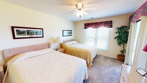 A hotel room with two beds, a ceiling fan, a window with blinds, a potted plant, and framed pictures on the wall. - River Creek 1 Unit 104 (Sunset Beach)