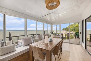 A spacious room with a large wooden table, comfortable seating, and large windows offering a view of the sea. - Waterfront Retreat on West Bay w Hot Tub, Games & More! 7345 (Traverse City)