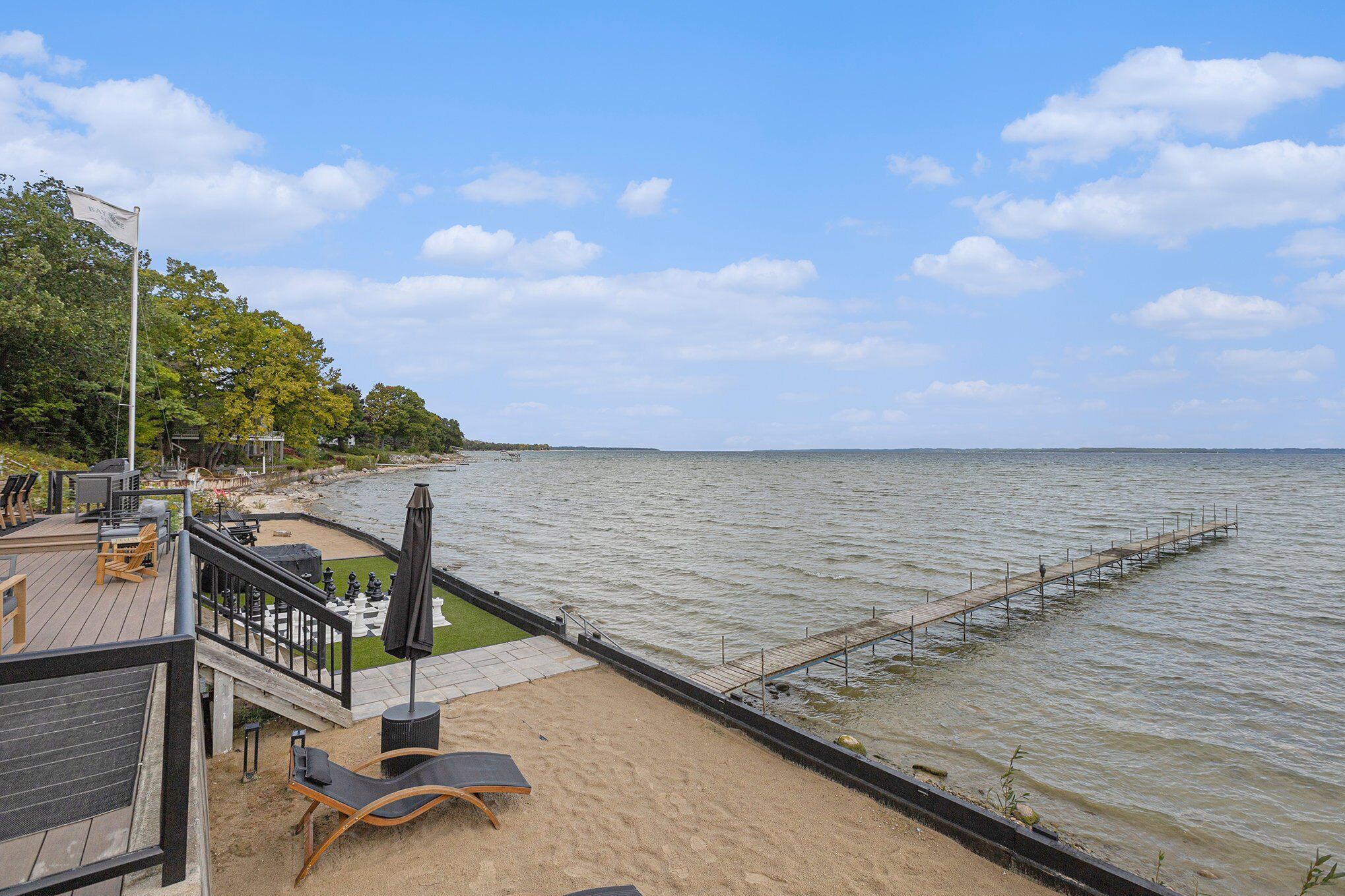A beachside deck with outdoor seating, a pier extending into the water, and a view of the sea.