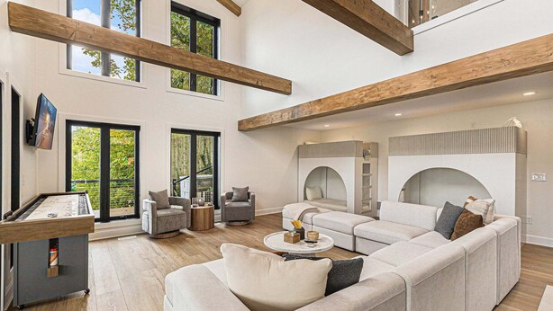 A spacious living area with a high ceiling, wooden beams, a large sofa, a coffee table, and a fireplace. - Waterfront Retreat on West Bay w Hot Tub, Games & More! 7345 (Traverse City)
