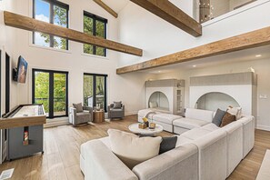 A spacious living room with a sectional sofa, a coffee table, and a pool table. There are large windows and a high ceiling with exposed beams. - Waterfront Retreat on West Bay w Hot Tub, Games & More! 7345 (Traverse City)
