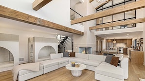 A spacious living area with a large sectional sofa, a round coffee table, and exposed wooden beams. - Waterfront Retreat on West Bay w Hot Tub, Games & More! 7345 (Traverse City)
