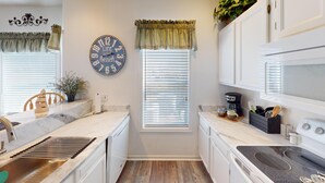 A compact kitchen with white cabinetry, a marble countertop, a clock, and a coffee maker. - River Creek 2 Unit 2002 (Sunset Beach)