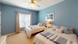 A bedroom with two beds, a ceiling fan, a window with curtains, a nightstand with a lamp, and a framed picture on the wall. - River Creek 2 Unit 2002 (Sunset Beach)