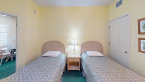 A small, cozy room with two single beds, a small table with a lamp, a chair, and a door. - Royal Poste Unit 2605 (Sunset Beach)