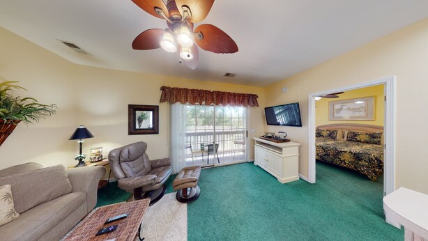 A living room with a green carpet, a brown leather chair, a sofa, a TV, and a bed with a floral bedspread. - Royal Poste Unit 2605 (Sunset Beach)