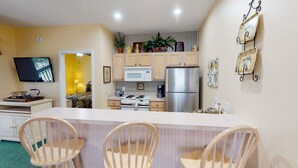 A compact kitchen with a microwave, stove, refrigerator, and wooden cabinets. There is a dining area with a table and chairs. - Royal Poste Unit 2605 (Sunset Beach)