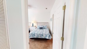 A bedroom with a bed, a nightstand, a lamp, and a door. - River Creek 2 Unit 1802 (Sunset Beach)