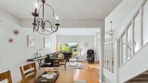 Amplia sala de estar con mesa de comedor de madera, un sofá y un mecedora para bebé. Un candelabro cuelga del techo, y hay cuadros enmarcados en las paredes.