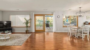 Una sala de estar amplia con un televisor de pantalla plana, un comedor con mesa y sillas, y un gran ventanal corredero que da a un patio.