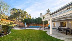Un patio trasero con piscina, un porche techado y una cerca de madera.
