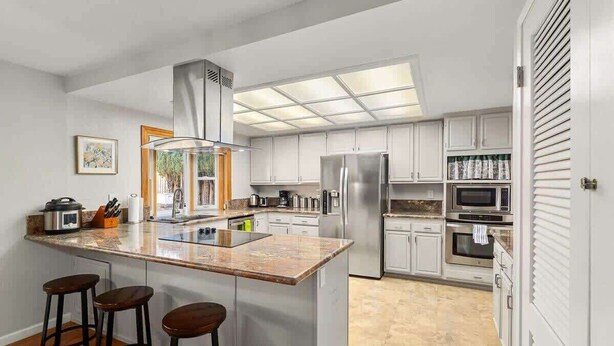 Una cocina moderna con una isla central, electrodomésticos de acero inoxidable y un amplio ventanal que proporciona luz natural.