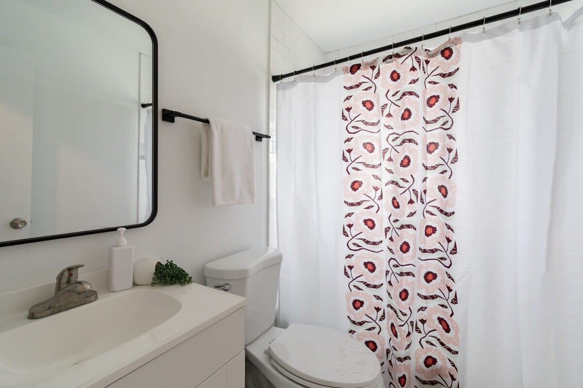 Un baño con lavamanos blanco, un espejo, inodoro y cortina de ducha con motivos florales.