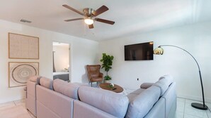 A modern living room with a sectional sofa, a ceiling fan, a flat-screen TV, and a floor lamp. - Fillmore Unit 11 (Cape Canaveral)