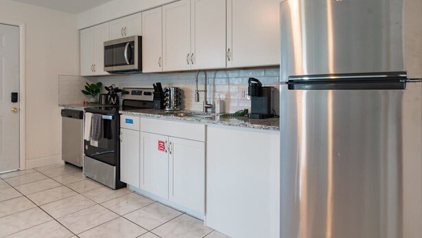 A modern kitchen with white cabinets, stainless steel appliances, and a tiled floor. - Fillmore Unit 11 (Cape Canaveral)