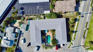 An aerial view of a residential area with a central building featuring a swimming pool, surrounded by parked cars and greenery. - Fillmore Unit 11 (Cape Canaveral)
