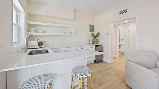 Una cocina moderna con armarios blancos, una isla grande con taburetes y vista al baño contiguo.