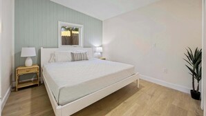 Un dormitorio con cama, mesitas de noche, una ventana y una planta en maceta.