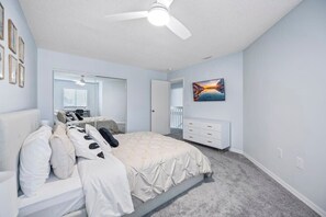Ein Schlafzimmer mit einem Bett, einem Schminktisch, einem Deckenventilator, einem Spiegel und einem Bild an der Wand.
