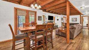 A spacious living area with a wooden ceiling, a dining table with chairs, a sofa, and a television mounted on the wall. - Otter Hot Tub Retreat Near Sharc (Bend)
