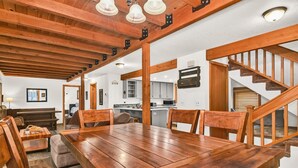 A spacious dining area with a wooden table and chairs, a kitchen in the background, and a staircase leading to an upper level. - Otter Hot Tub Retreat Near Sharc (Bend)