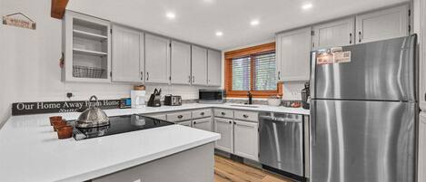 A modern kitchen with white cabinets, stainless steel appliances, and a wooden floor.