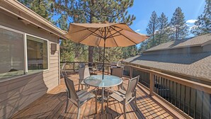 Une terrasse en bois avec une table et des chaises en verre, un parasol et un barbecue.
